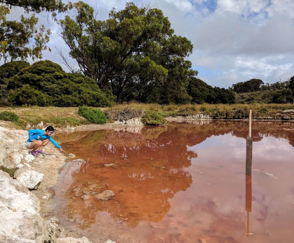 Jackie Szeto, Life Of Doing, points to the Pink Lake at Rottnest Island, Australia.