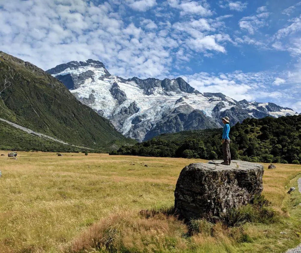 New Zealand Road Trip: Jackie Szeto, Life Of Doing, stands on a giant rock on Hooker Valley Track in Aoraki/Mount Cook National Park