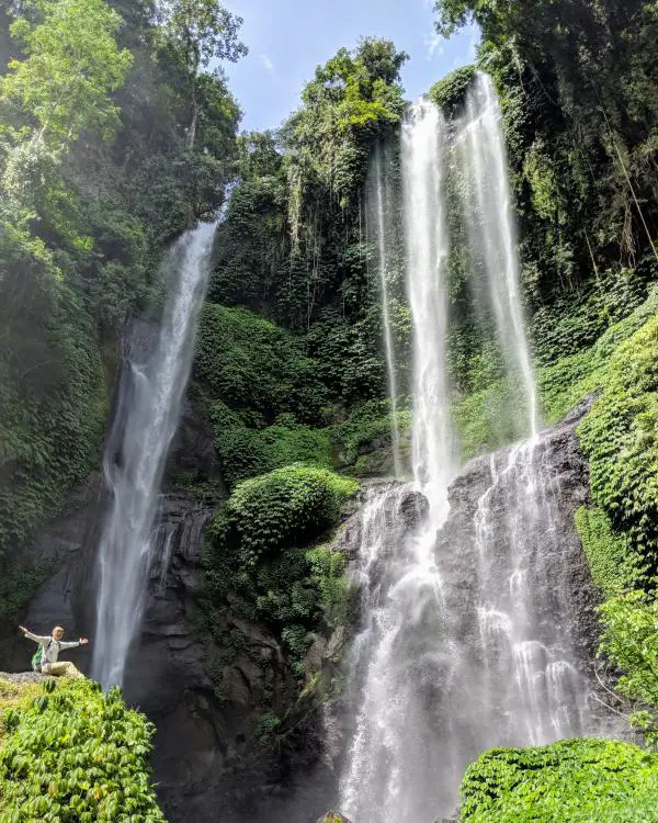 Justin Huynh, Life Of Doing, sits on a rock with the Sekumpul Waterfall in the background.