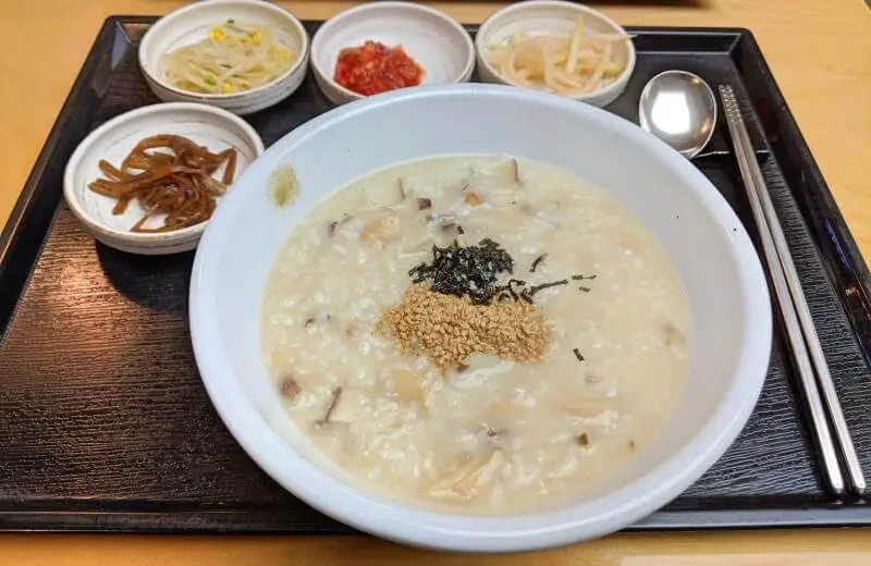 A black tray with a bowl of abalone porridge and four small side dishes at Migabon in Myeongdong, Seoul, South Korea  