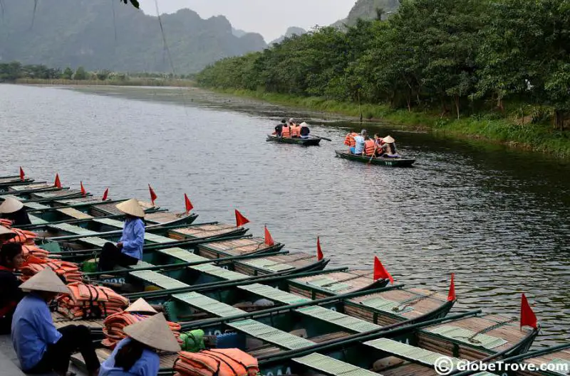 Local rowers wait in their boat until it has a full capacity of four riders. There are two boats in the distance as they head to the karst landscapes in Trang An, Vietnam.