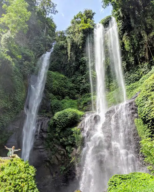 Justin Huynh, Life Of Doing, sits on top of a rock to get a photo with the Sekumpul Waterfall in North Bali. There are three cascading falls surrounded by a luscious forest.