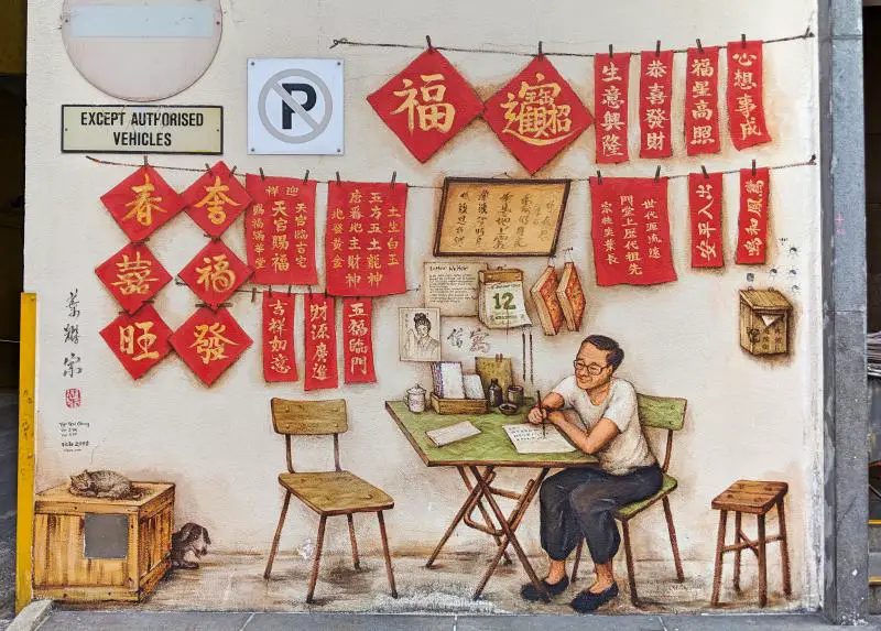 One of the street art in Singapore's Chinatown. An older gentleman is shown writing calligraphy. He is surrounded by red signs written in gold letters for good fortune.