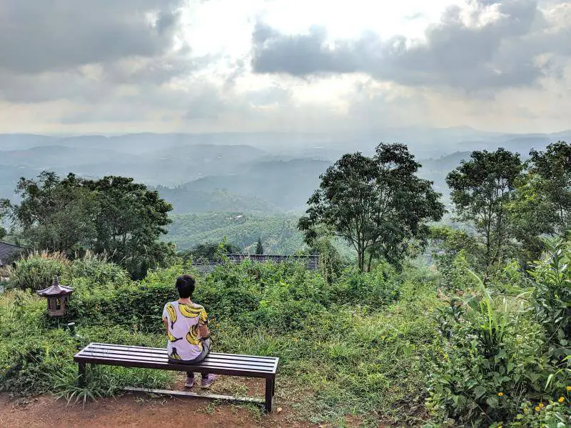 Jackie sitting on a bench while overlooking the green mountainside at Linh Quy Phap An Pagoda in Bao Loc, Vietnam.