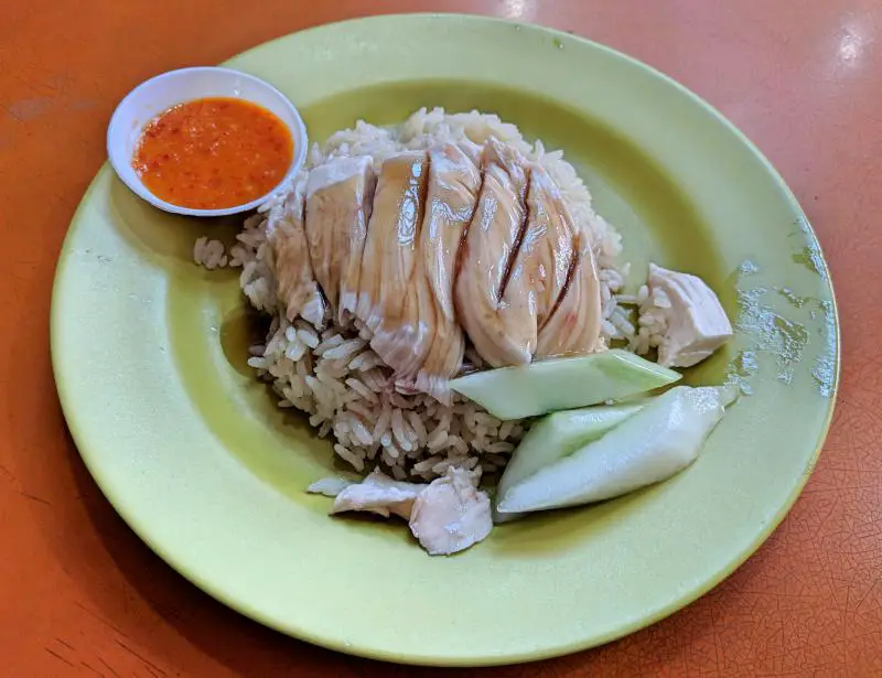 A small plate of Hainanese style chicken and rice with a side of sweet chili sauce located at Tian Tian Hainanese Chicken Rice in Maxwell Food Centre, Singapore.