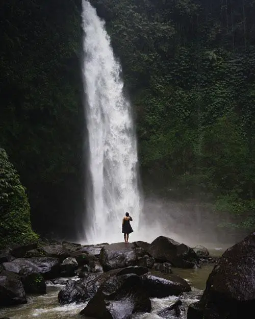 A woman wearing a dress poses in front of the Nungnung Waterfall in Bali, Indonesia. Check out this post to learn more about the best waterfalls in Bali.