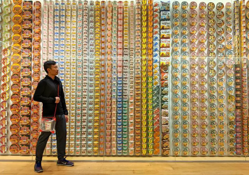 Justin from Life Of Doing gazes at the wall of Nissin Cup Noodles and the international ramen at the Yokohama Cup Noodles Museum. He is also holding a customized Cup Noodles.