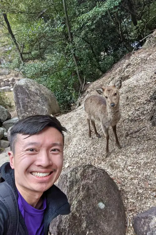 Justin Huynh from Life Of Doing poses next to a deer on the Mount Misen hike in Miyajima, Japan.