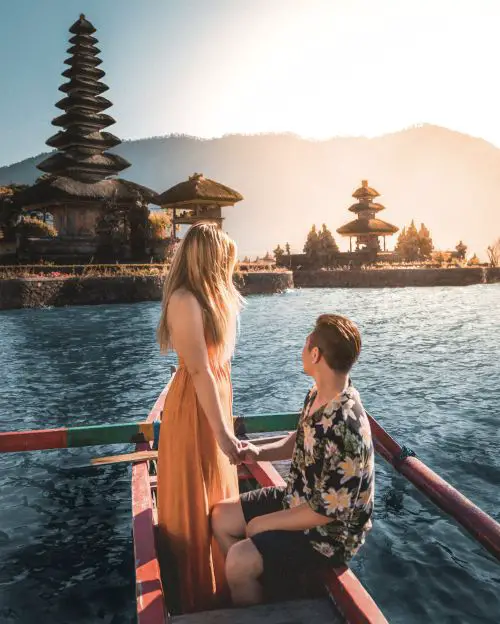 A woman and man ride a wooden boat while overlooking the Pura Ulun Danu Beratan in Bali, Indonesia