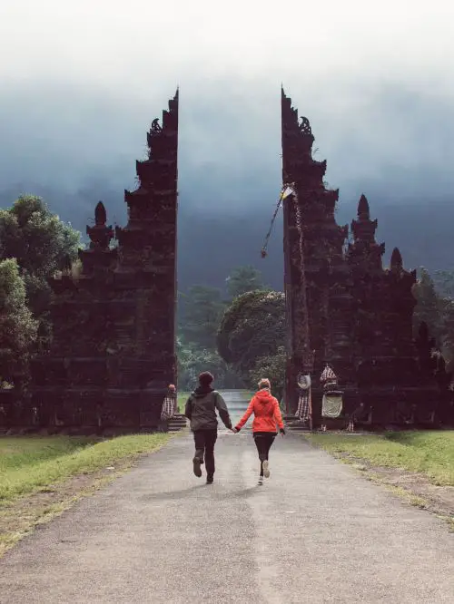 A man and woman run towards the entrance of the Handara Gate in Bali