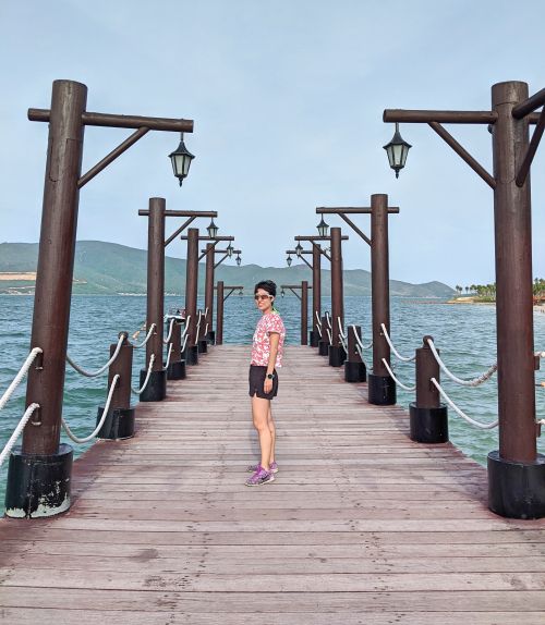 Jackie Szeto, Life Of Doing, stands on the Hon Tam Pier with the ocean in the background.