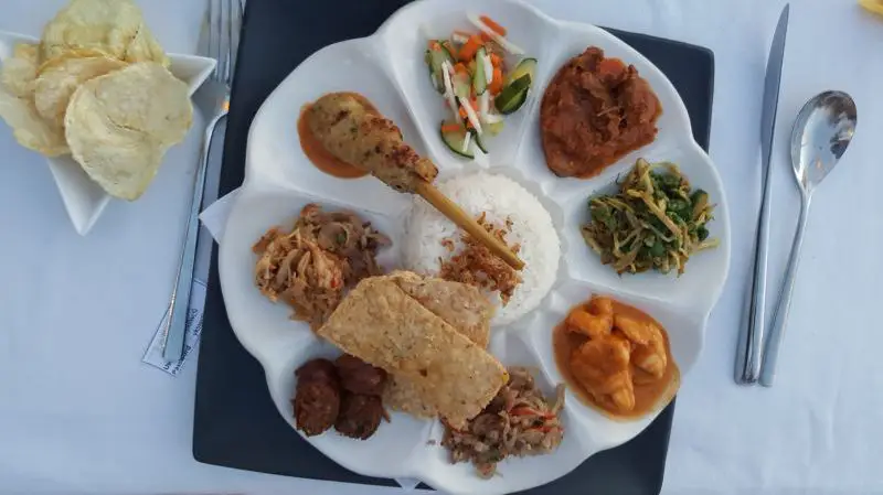 A plate of nasi campur which has a skewer, rice, meat, and vegetables