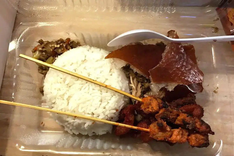 Takeout container of rice with suckling pig and skewers from Karya Rebo