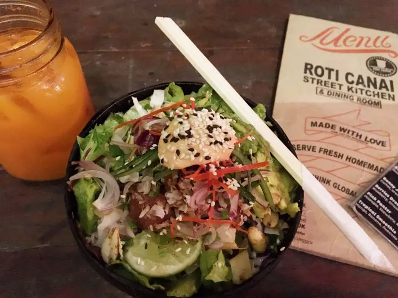A bowl of poke with rice, salad, and fresh fish and a cup of fresh juice