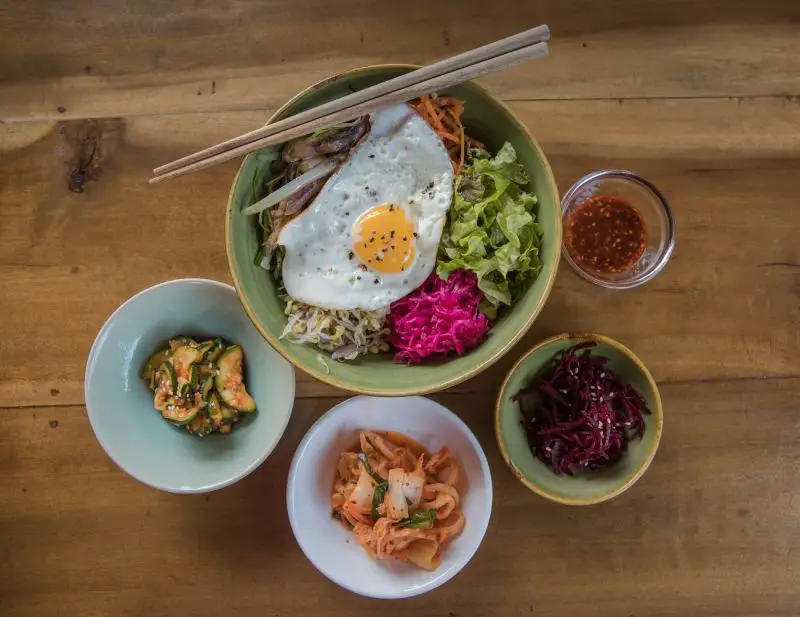 Bowl of rice with pickles, fried egg, and vegetables and three small side dishes of kimchi and pickles