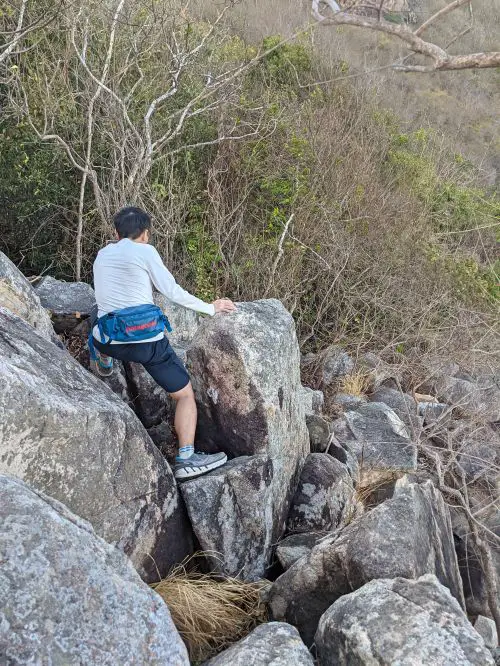 Justin Huynh, Life Of Doing, climbs down the giant grey rocks to continue on the Big Mountain Vung Tau hiking trail.