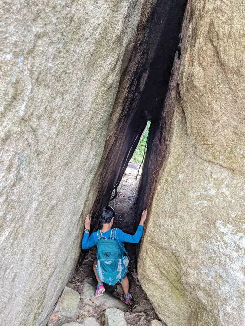 Jackie Szeto, Life Of Doing, enters a small cave opening and holds onto both sides of the rocks.