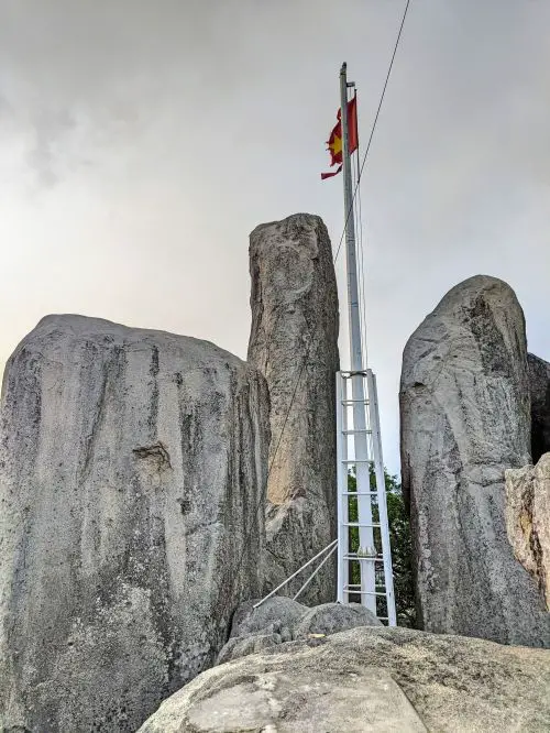 A flagpole with a Vietnamese flag is perched on top of grey rocks on Nui Minh Dam Mountain.