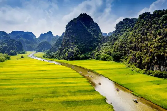 A river with sampan boats flows between green fields and limestone karsts in Ninh Binh, one of the best places to visit in Vietnam.