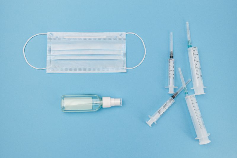 A face mask, four syringes, and an empty spray bottle on a blue background