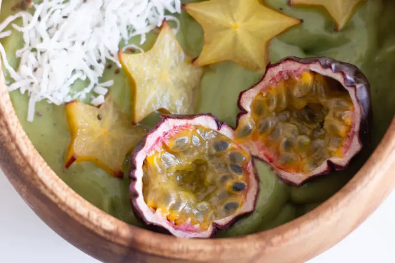 A green smoothie bowl with shredded coconut flakes, star fruit, and passion fruit.