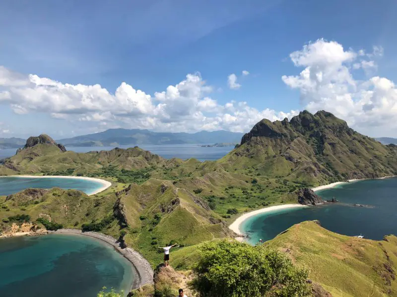A person with the arms wide open with hills and three blue lakes at Padar Island, Indonesia