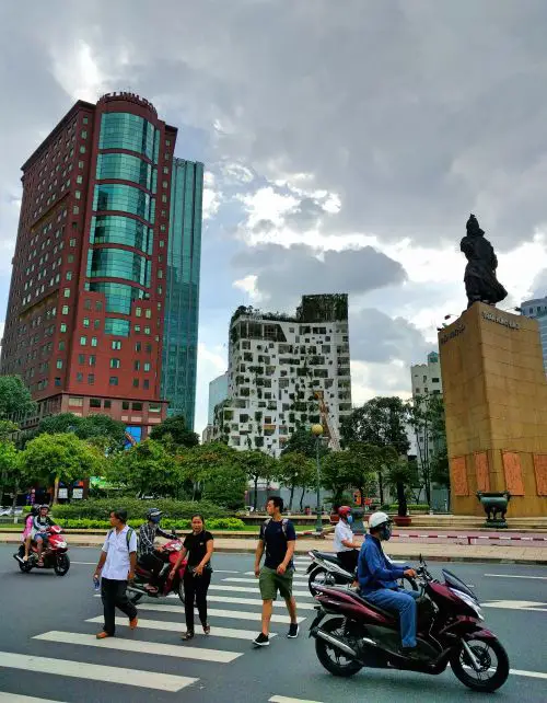 Three people cross the streets with motorbikes passing by in Ho Chi Minh City, Vietnam