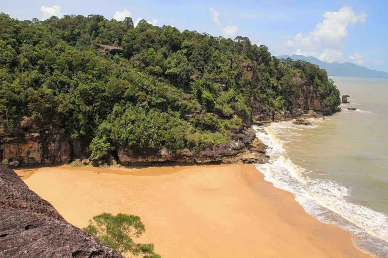 A golden sand beach next to the ocean and surrounded by green mountains at Bako National Park, Borneo, Malaysia