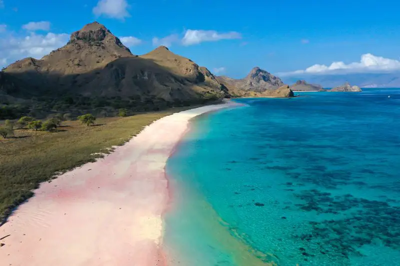 A pink sandy beach next to mountains and blue ocean in Komodo National Park, Indonesia, one place to visit in Asia during the summer season.