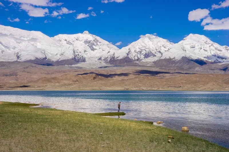 A person standing next to the lake with snowy mountains in the backdrop in Kashgar, China