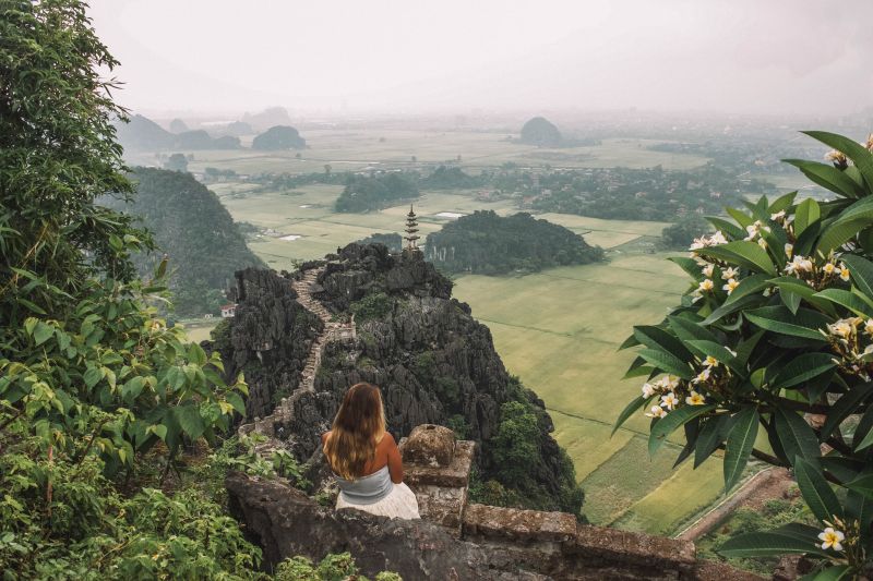 A woman wearing a white dress leaning against the walls and overlooking the temple and green fields in Ninh Binh, Vietnam