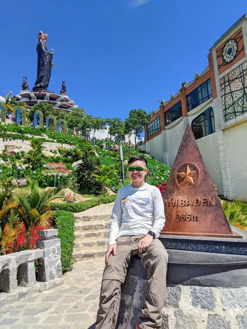 Justin Huynh, Life Of Doing, sitting in front of the Nui Ba Den triangle landmark at 986 meters at Sun World Ba Den in Tay Ninh, Vietnam