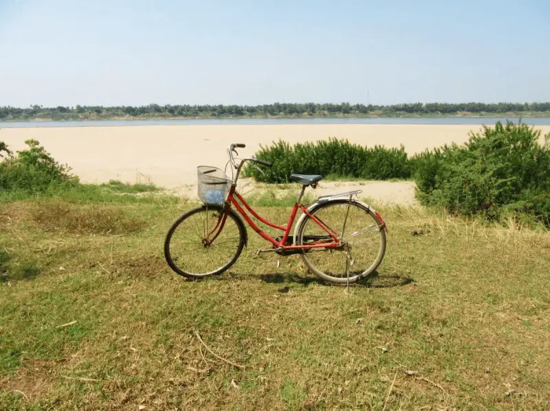 A red bicycle parked next to a white sandy beach on Koh Trong, Cambodia