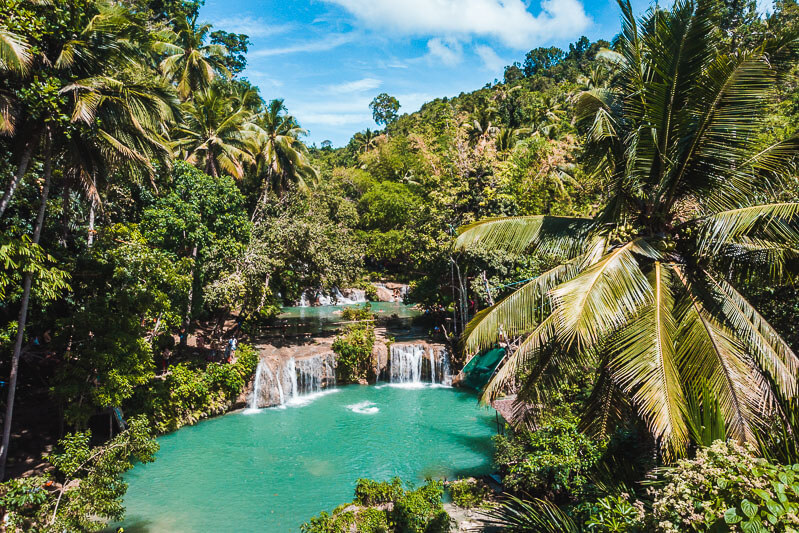 Two-tier cascades of Cambugahay Waterfalls surrounded by palm trees and jungles in Siquijor, Philippines
