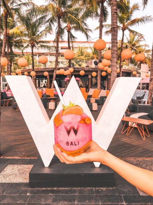 A hand holding a W Bali branded coconut drink in front of a W sign at Woobar in Bali, Indonesia