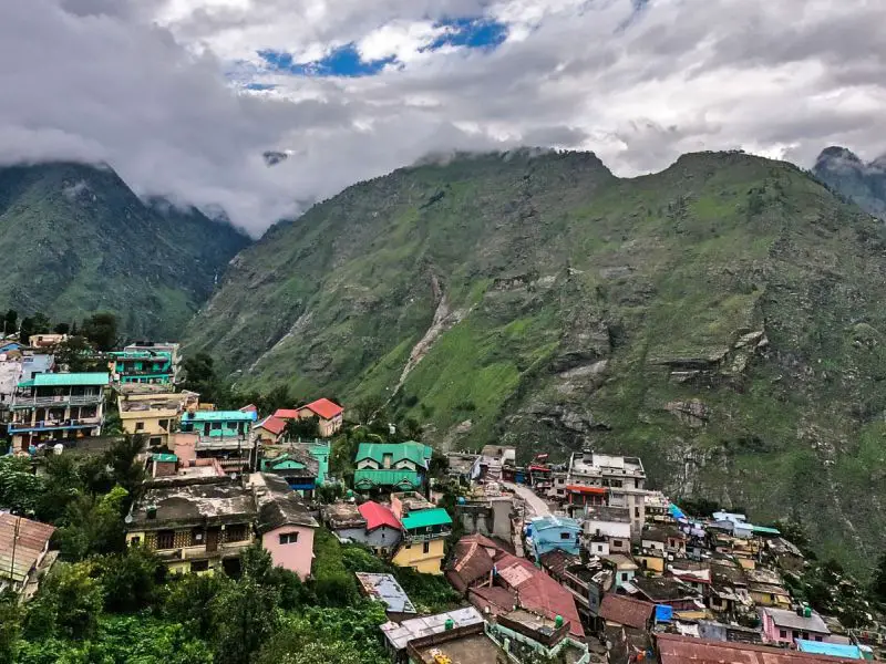 A tall green mountain slope has a valley of houses in Uttarakhand, India