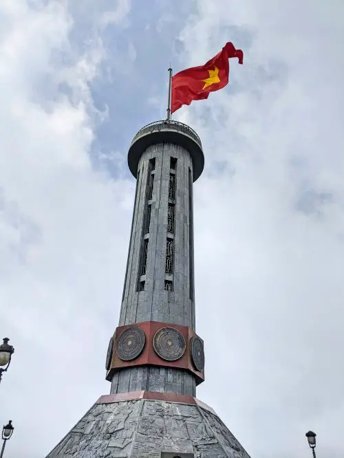A flag pole with the Vietnamese flag of red flag and yellow star in the sky
