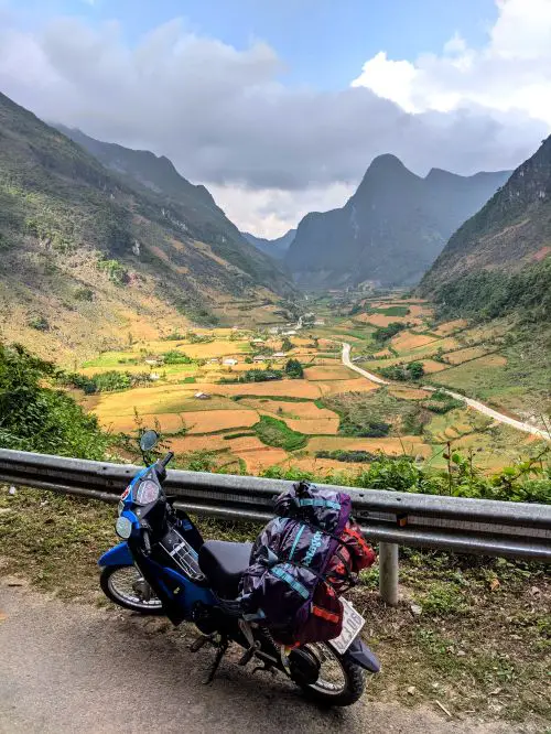 A parked motorbike is in front of the valley with rice fields and mountains