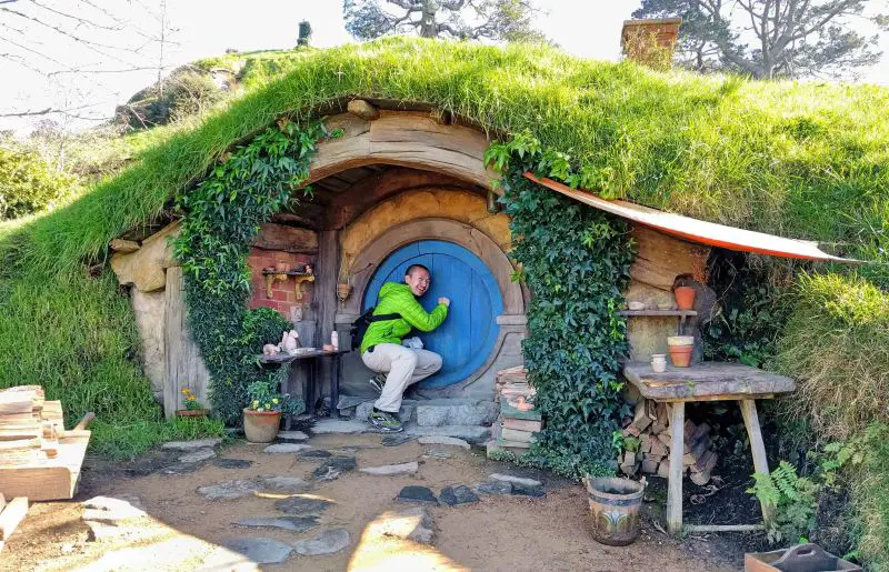 Justin Huynh, Life Of Doing, knocks on a blue door of a Hobbit hole at Hobbiton Movie Set