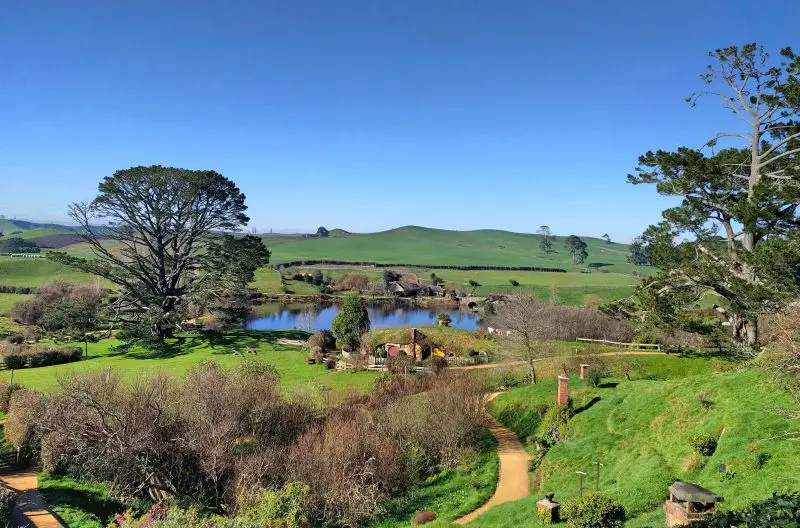 View of the Hobbiton Movie Set with the green hills and lake.