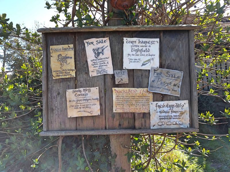 Various signs on a signboard such as wheelbarrow, fiddle, smoke ring contest, and fresh eggs at Hobbiton Movie Set