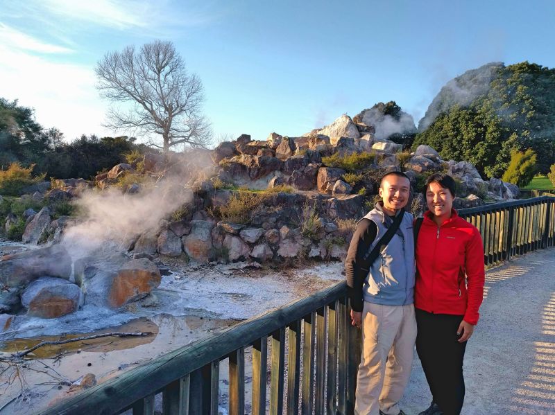Justin Huynh and Jackie Szeto, Life Of Doing, stand in front of a geothermal springs with steams coming up at Kuirau Park in Rotorua, New Zealand