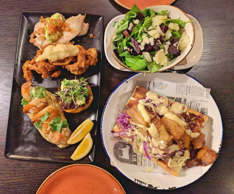Three plates of food - pork belly po boy sandwich, seafood platter, and salad, at Onehunga Cafe in Auckland, New Zealand