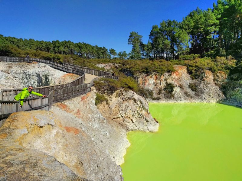 Justin Huynh, Life Of Doing, points to the neon green geothermal lake at Wai-O-Tapu Thermal Wonderland in Rotorua