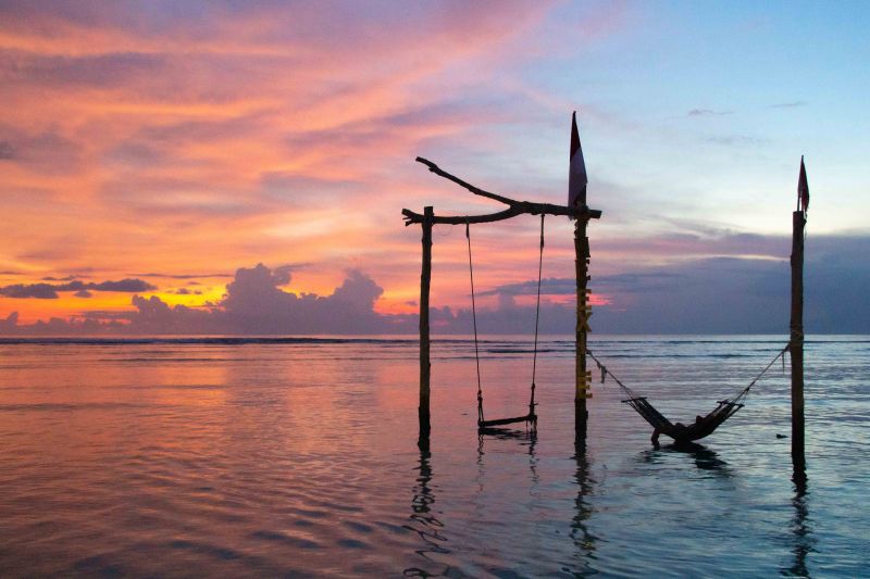 A person lying on a hammock in the waters of Gili Trawangan with the orange and pink sunset