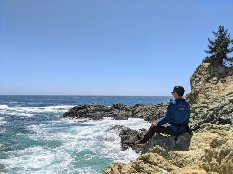 Justin Huynh, Life Of Doing, sits on a rock and looks at the ocean views of Partington Cove in Big Sur, California