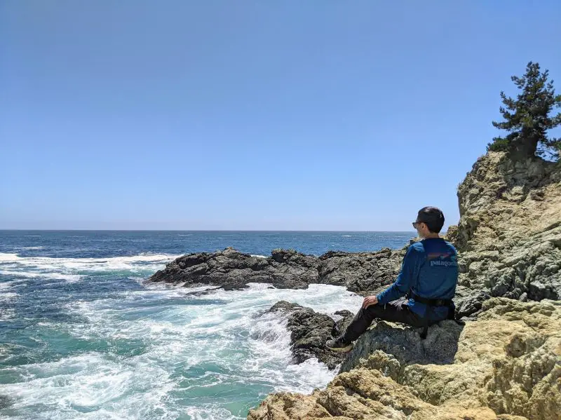 Justin Huynh, Life Of Doing, sits on a rock and looks at the ocean views of Partington Cove in Big Sur, California