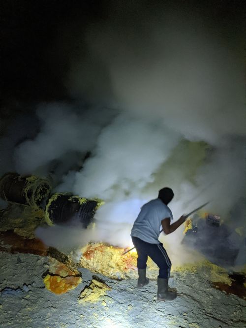 A miner using a rod to break the yellow sulfur at Ijen Crater, Indonesia