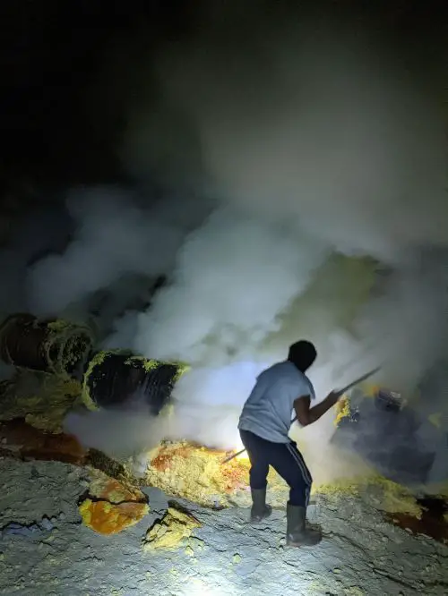 A miner using a rod to break the yellow sulfur at Ijen Crater, Indonesia