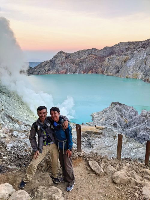 Justin Huynh and Jackie Szeto, Life Of Doing, stand in front of the Ijen Crater with the turquoise lake in the back